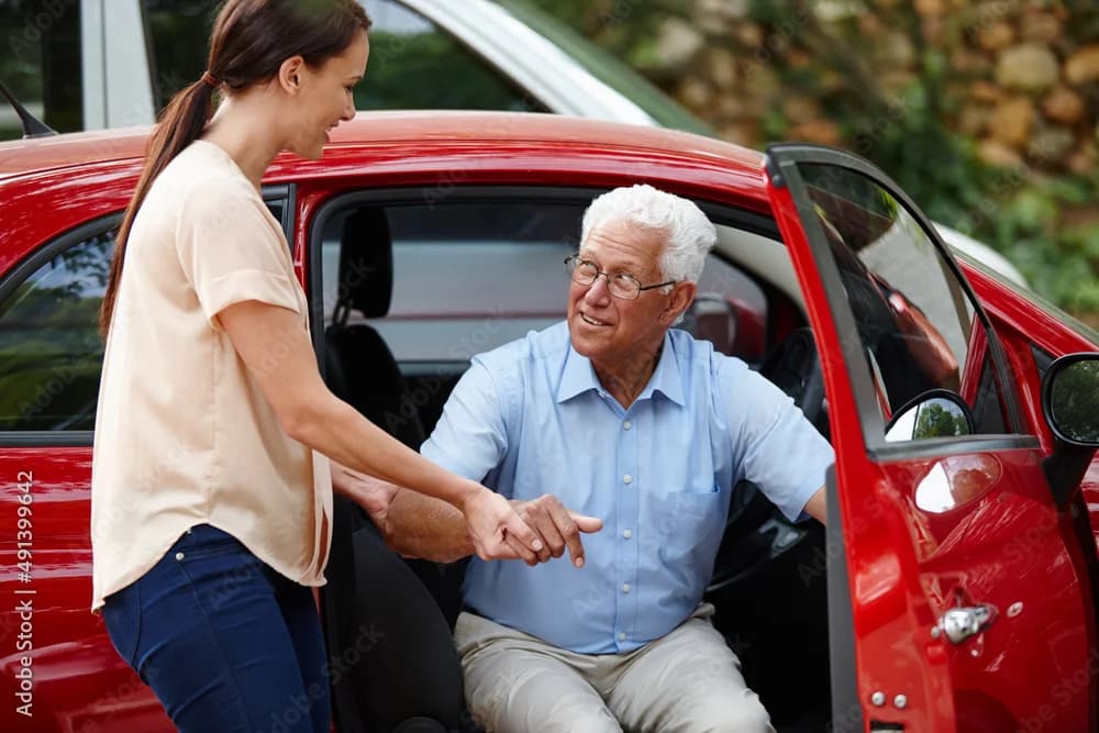 Caregiver assisting an older adult into a car for a medical appointment